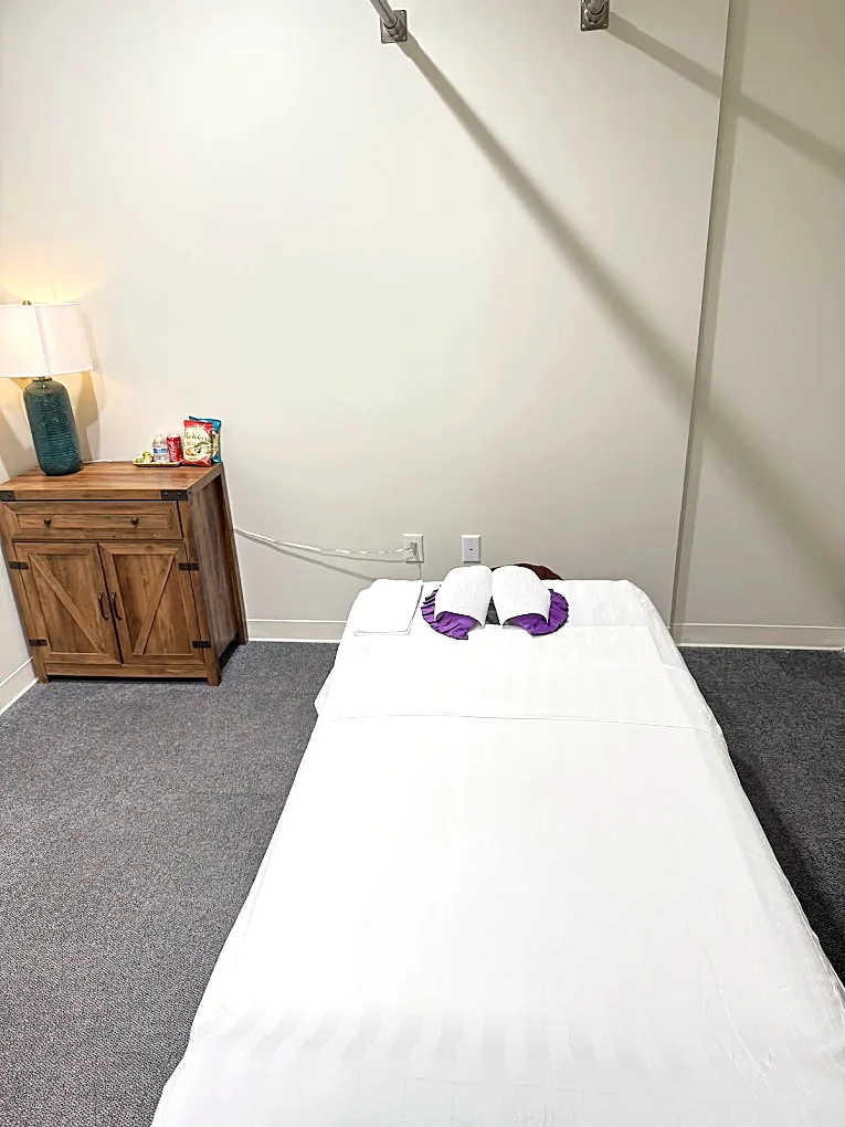 A made-up massage table with folded white towels and a low lamp in a treatment room at Spring Massage